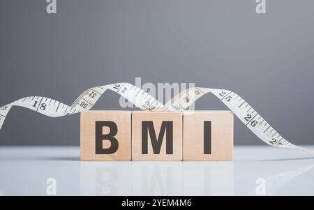 Blocco di legno con "BMI" accanto a un metro a nastro. L'immagine simboleggia il concetto di Indice di massa corporea, evidenziando l'importanza della salute Met Foto Stock