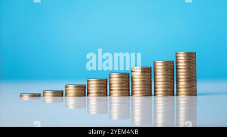 Vaso di vetro pieno di monete e una piccola piantina al centro, con pile di monete disposte dal più piccolo al più grande su un tavolo. Evidenzia la conc Foto Stock