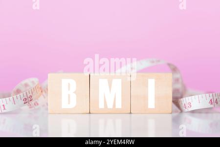Blocco di legno con "BMI" accanto a un metro a nastro. L'immagine simboleggia il concetto di Indice di massa corporea, evidenziando l'importanza della salute Met Foto Stock
