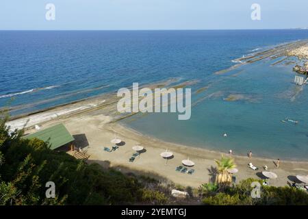 Le onde si infrangono dolcemente sulla riva mentre i bagnanti si godono l'atmosfera tranquilla della spiaggia e le acque cristalline nelle vicinanze. Foto Stock