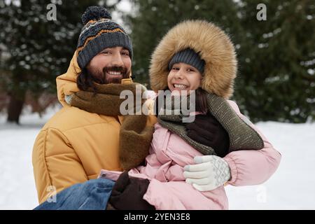 Indossa il ritratto del padre felice che tiene in braccio la figlia mentre giochi all'aperto in inverno e sorridi con gioia alla fotocamera Foto Stock