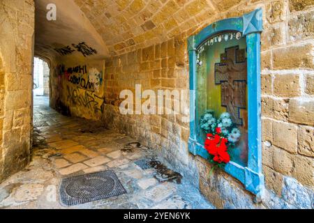 Un piccolo santuario sotto lo storico Arco del Crocefisso a Bari Vecchia, adornato di fiori e graffiti locali. Foto Stock