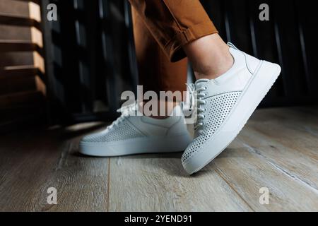 Gambe femminili sottili in pantaloni da primo piano in sneaker casual bianche. Scarpe da donna in pelle. Foto Stock