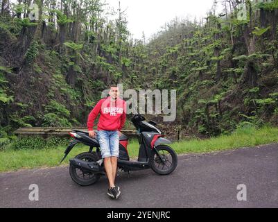 Uomo in moto sulla strada in montagna con palme sullo sfondo. Bali, Indonesia - 08.03.2018 Foto Stock