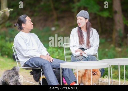 Un uomo coreano e una donna giapponese, entrambi di 30 anni e una coppia sposata, stanno godendo un brunch autunnale con tre cani in un elegante caffè situato in Foto Stock