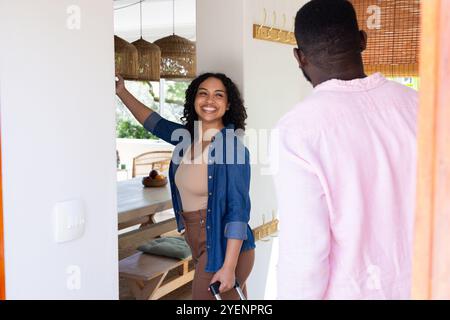 Coppia multirazziale sorridente, con valigia, gioia, a casa. ospitalità, tecnologia, allegro, felicità, stile di vita, comunicazione Foto Stock