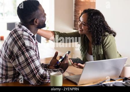 Felice coppia multirazziale a casa per condividere i momenti con smartphone e laptop. Tecnologia, stile di vita, connettività, relazione, comunicazione, dispositivo Foto Stock