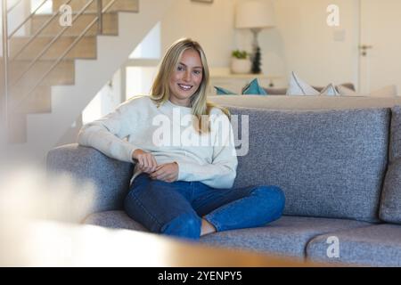 Donna sorridente che si rilassa sul comodo divano di casa, godendosi un pomeriggio tranquillo. Relax, stile di vita, tempo libero, comfort, benessere, tranquillità Foto Stock