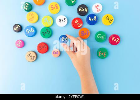 Mani dei bambini che sistemano tappi colorati per bottiglie con problemi di moltiplicazione su sfondo blu. Concetto educativo Flat Lay per l'apprendimento e i giochi di matematica Foto Stock