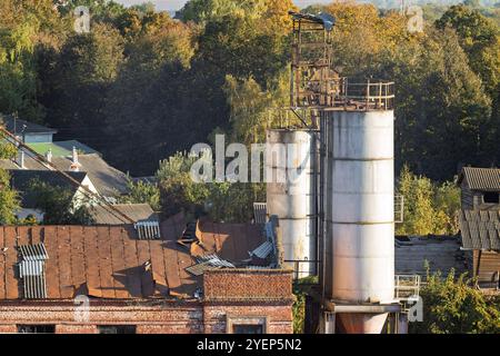 Vecchio edificio industriale abbandonato con tetto arrugginito e struttura decaduta. I fogli di cartone ondulato sono sparsi sul tetto, sottolineandone la divergenza Foto Stock