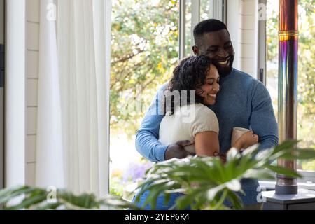 Coppia multirazziale felice che si abbraccia a casa, godendosi momenti intimi con un caffè. amore, romanticismo, intimo, legame, stile di vita Foto Stock