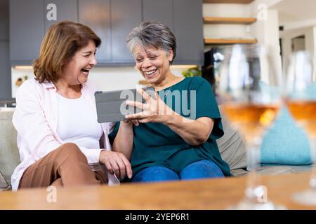 Amiche di sesso femminile che ridono insieme a casa mentre guardano lo schermo di un tablet. Amicizia, tecnologia, anziani, tempo libero, stile di vita, incollaggio Foto Stock
