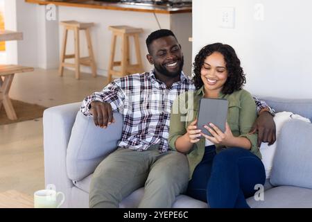 Felice coppia multirazziale che si rilassa sul divano e si diverte con un tablet a casa. relax, unione, digitale, stile di vita, tecnologia, accogliente Foto Stock
