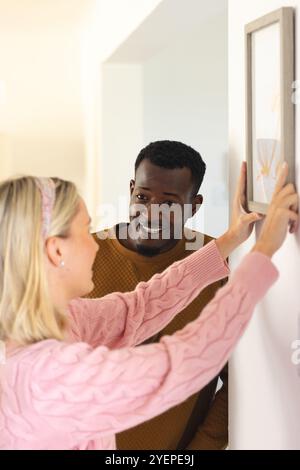 coppia multirazziale appesa foto a casa, sorridendo e godendo di decorazioni natalizie. Celebrazione, arredamento per la casa, stile di vita, legame, partnership, festivi Foto Stock