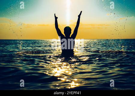 Foto colorata della silhouette di Happy Man con le mani in alto nel mare Foto Stock