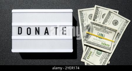 Cartone luminoso con parole DONATE in lettere nere intorno alle banconote in dollari USA. Soldi, affari, finanza, investimento, risparmio. Fattura in contanti. Budget aziendale Foto Stock