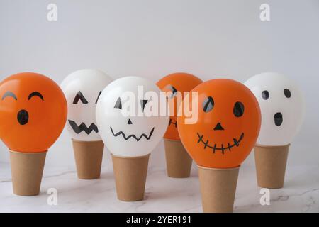 La faccia di Jack dipinta sulle bollature. Preparazione di palline bianche e arancioni fai da te per la festa di Halloween. Halloween attività a casa. Giocattoli fatti a mano Artigianato per bambini Foto Stock