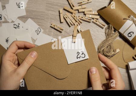 Una giovane donna irriconoscibile indossa il numero sulla borsa artigianale, si chiude con il clothespin. Carta kraft femminile per il calendario dell'avvento fatto in casa, realizzata con il tuo Foto Stock