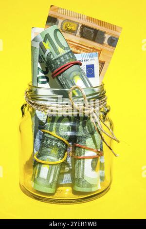 Vasetti di vetro riempiti di banconote in euro, risparmio all'interno del vaso di vetro, denaro isolato su sfondo giallo, spazio per la copia del testo. Nota cartacea. Budget aziendale di Foto Stock