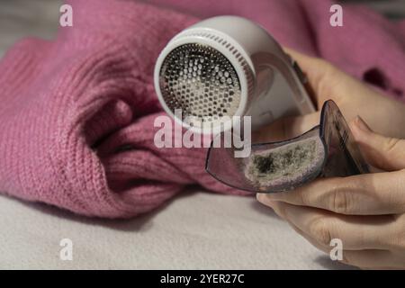 Donna che usa un rasoio anti-pilling a casa. Dispositivo per la rasatura degli abiti. Rasoio in tessuto anti-peluche. Rimuovi pelucchi per disappannamento con maglione portatile elettrico Foto Stock