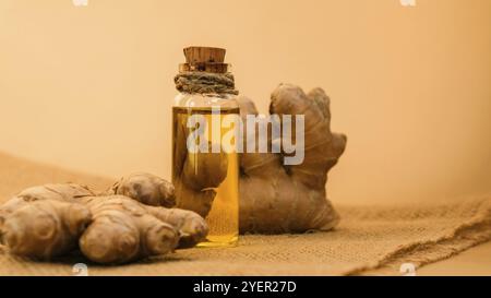 Bottiglia di vetro di olio essenziale di zenzero, radice di zenzero su sfondo beige. Concetto di cibo sano. Olio essenziale Zingiber officinale. Toni di terra Nat Foto Stock