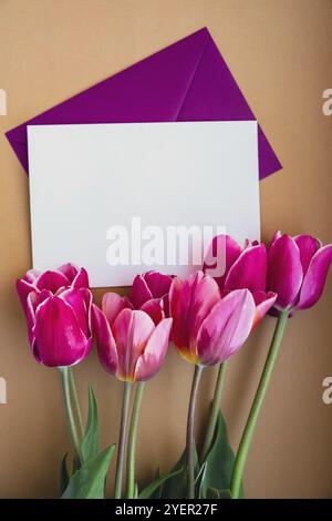 Spazio vuoto per la copia di una busta bianca per il testo o il design con un bellissimo bouquet di tulipani rosa su sfondo beige. Modello per le vacanze primaverili gre Foto Stock