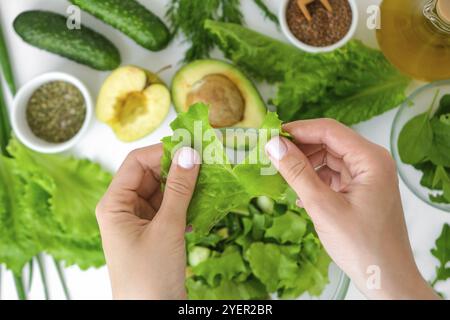 Insalata di cucina donna di verdure fresche verdi ed erbe. Cucina dieta sana o cibo vegetariano. Insalata femminile tagliata a mano circondata da verdure verdi Foto Stock