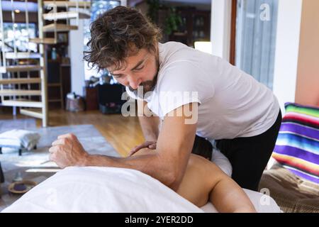 Massaggiatore professionale di media età che offre massaggi terapeutici al suo cliente. Giovane donna che gode di un rilassante massaggio alla schiena in un ambiente accogliente casa Foto Stock