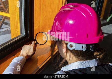 Primo piano su un ispettore donna che utilizza una lente d'ingrandimento durante l'ispezione della qualità dell'aria, alla ricerca di muffe o problemi di funghi sui bordi della finestra in legno Foto Stock