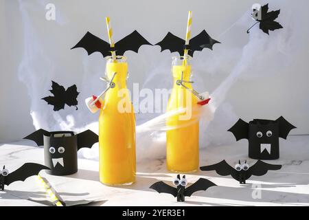 Halloween mocktails. Cocktail analcolico all'arancia per la festa di Halloween sul tavolo bianco. Le paillette sono decorate con pipistrelli di carta tagliati. Halloweens Spooky dri Foto Stock