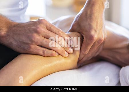 Massaggio e cura del corpo. Donna sdraiata e rilassante al massaggio in un ambiente accogliente casa. Mani forti di massaggiatore maschile professionale che fanno un massaggio delicato Foto Stock