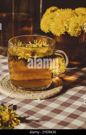 Dente di leone fiore tè sano in teiera di vetro e bicchiere di vetro sul tavolo. Delizioso tè alle erbe da fiori di dente di leone fresco a casa il giorno d'estate. Verde cl Foto Stock