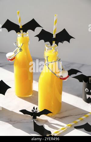 Halloween mocktails. Cocktail analcolico all'arancia per la festa di Halloween sul tavolo bianco. Le paillette sono decorate con pipistrelli di carta tagliati. Halloweens Spooky dri Foto Stock