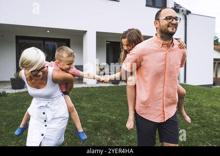 Felice famiglia caucasica di quattro persone, madre padre e figli a casa, all'aperto che gioca sull'erba e all'interno del soggiorno divertendosi come un fami Foto Stock