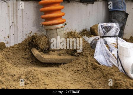 Vista ravvicinata sulla piastra metallica di un pestello vibrante, con sabbia che salta in aria dall'azione pesante della macchina, del terreno e della preparazione Foto Stock