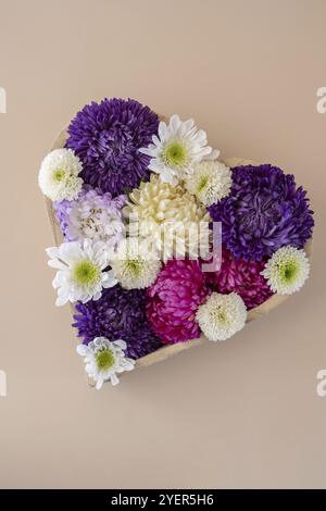 Fiori colorati misti a forma di cuore su sfondo beige. Concetto di giorno dell'amore e delle valenze, diserbo, anniversario. Modello cartolina di auguri Foto Stock