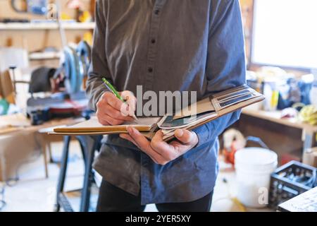 Ispettore che tiene in mano un taccuino durante un'ispezione a domicilio in garage, primo piano e attenzione selettiva di un uomo che prende appunti professionali Foto Stock