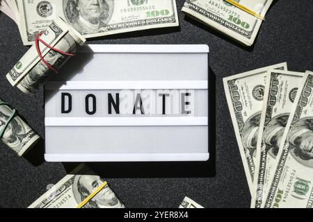 Cartone luminoso con parole DONATE in lettere nere intorno alle banconote in dollari USA. Soldi, affari, finanza, investimento, risparmio. Fattura in contanti. Budget aziendale Foto Stock