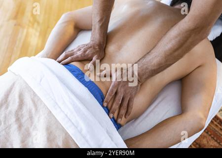 Un maschio irriconoscibile sdraiato sul tavolo e che riceve il massaggio alla schiena da un massaggiatore professionista. Vista dall'alto Foto Stock