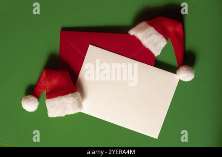 Berretto di Santa con busta vuota della nota della scheda di carta su fondo verde. Copiare lo spazio per il testo. Mock up per la pubblicità. Composizione di Natale di festa. Foto Stock