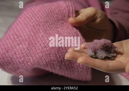Donna che usa un rasoio anti-pilling a casa. Dispositivo per la rasatura degli abiti. Rasoio in tessuto anti-peluche. Rimuovi pelucchi per disappannamento con maglione portatile elettrico Foto Stock