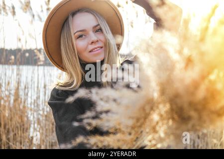 Donna bionda europea con cappello beige in pullover nero in campagna. Ora d'oro, cotagecore. Viaggi locali. Vita lenta. Salute mentale. Messa a terra a. Foto Stock