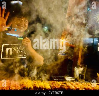 Un giovane giapponese che grigia spiedini al ristorante Washio Yakitori Izakaya a Chuocho, Kagoshima, Giappone. Foto Stock