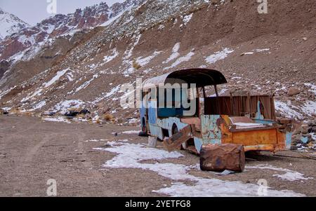 un vecchio autobus arrugginito si è rotto in disuso nel mezzo delle montagne con un po' di neve. trasporto abbandonato Foto Stock