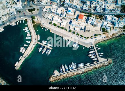 Vista aerea dall'alto di un drone della pittoresca cittadina con piccole case bianche in stile greco tradizionale e il porto marittimo con barche attraccate Foto Stock