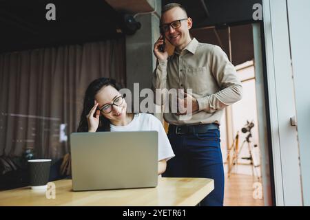 Un giovane uomo soddisfatto parla con una collega e si rallegra del lavoro svolto. I colleghi lavorano al computer portatile in ufficio. Lavorare in un ufficio moderno sp Foto Stock