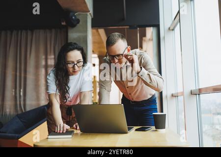 Un giovane uomo soddisfatto parla con una collega e si rallegra del lavoro svolto. I colleghi lavorano al computer portatile in ufficio. Lavorare in un ufficio moderno sp Foto Stock
