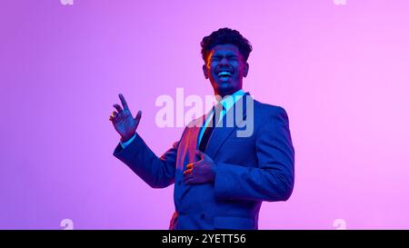 Ritratto di un giovane indiano gioioso in costume, che ride allegramente sullo sfondo rosa dello studio alla luce del neon Foto Stock