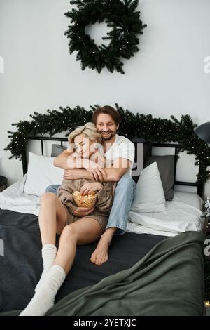 Una coppia abbraccia affettuosamente mentre condivide gli spuntini nella loro accogliente camera da letto, avvolti dal calore. Foto Stock