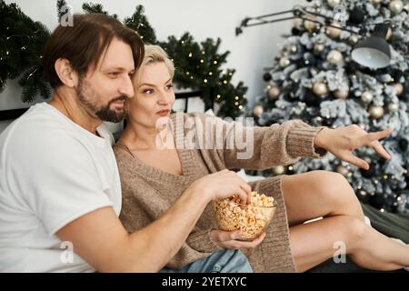 Una coppia si rilassa a casa, condividendo una ciotola di popcorn mentre guarda qualcosa insieme. Foto Stock